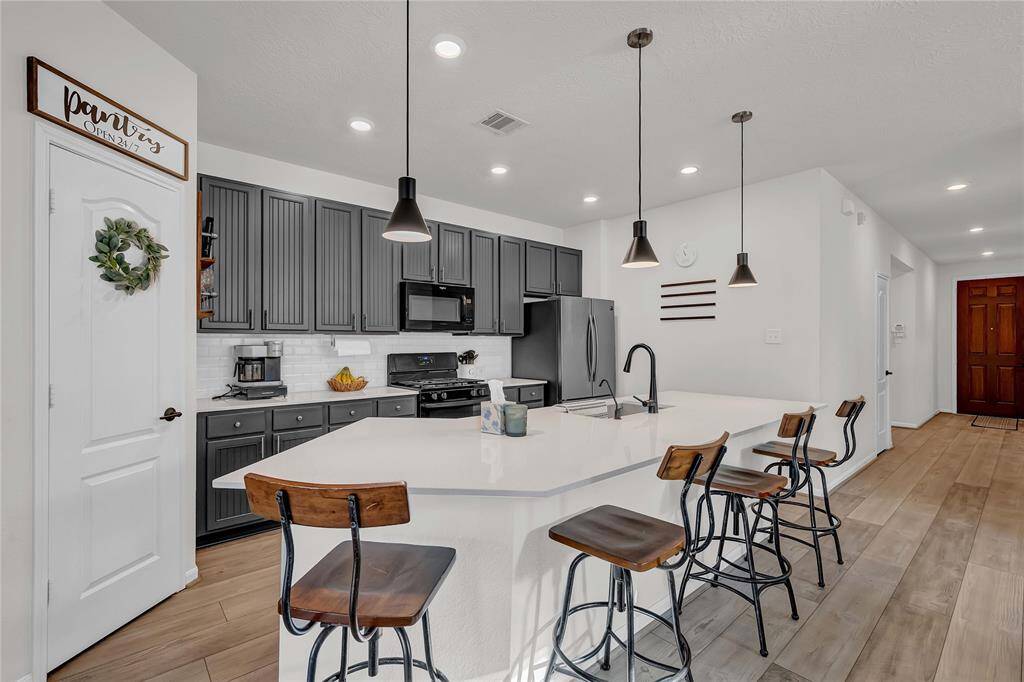This kitchen features modern gray cabinetry, stainless steel appliances, and a spacious white island with seating for four. Pendant lighting adds a stylish touch, while wood flooring enhances warmth.