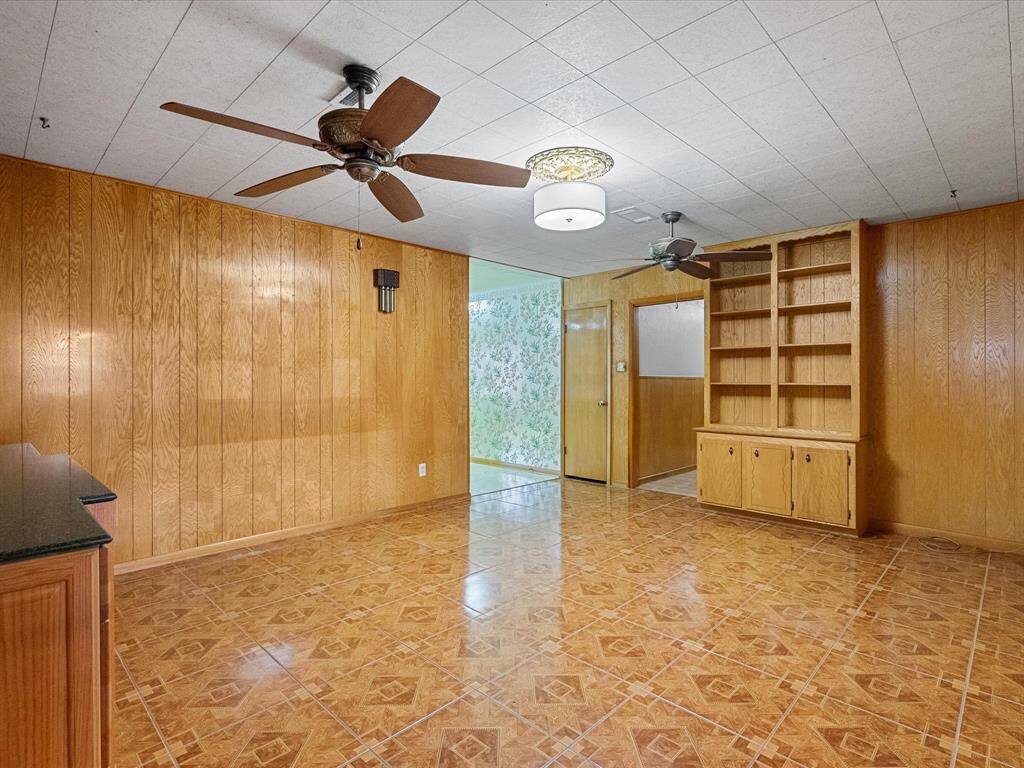 Featuring wood-paneled walls and tiled flooring, this space creates a warm and classic atmosphere. Included are custom built-in shelving and two ceiling fans for comfort. The space is versatile, yet ideal for a family room.