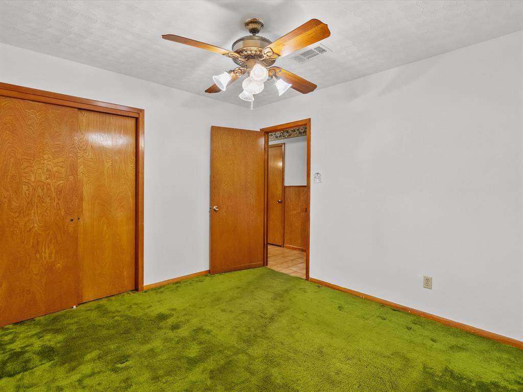 One of three secondary bedrooms, the room features neutral walls, wooden closet doors, and lighted ceiling fan. The walls are painted white, and there's a wooden door leading to another area of the house.