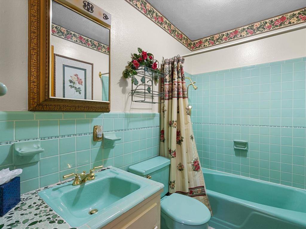 Charming hallway bathroom features vintage aqua green tiling fixtures, complemented by floral wallpaper & decor, and tile countertop in excellent condition all lend a cozy, nostalgic feel.