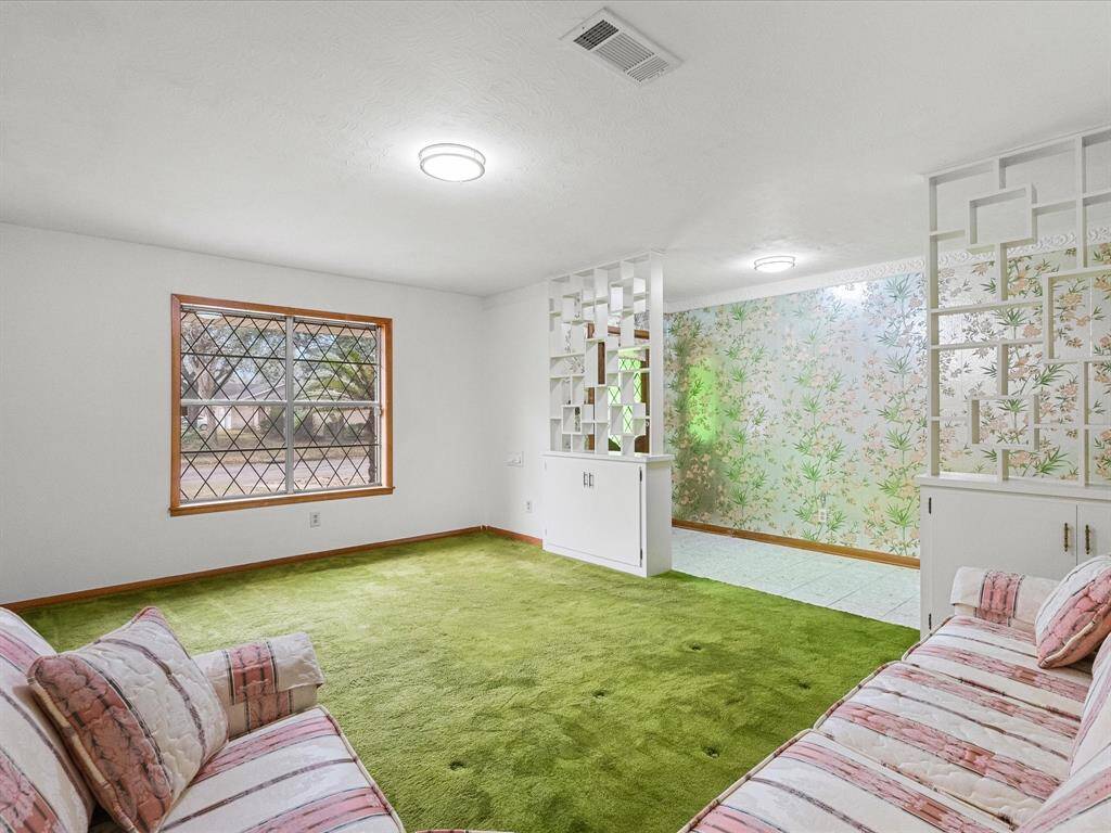 This room features a cozy, retro style with green carpet and floral wallpaper. It has ample natural light from a large window with a lattice design. Decorative wall dividers enhancing its unique charm.