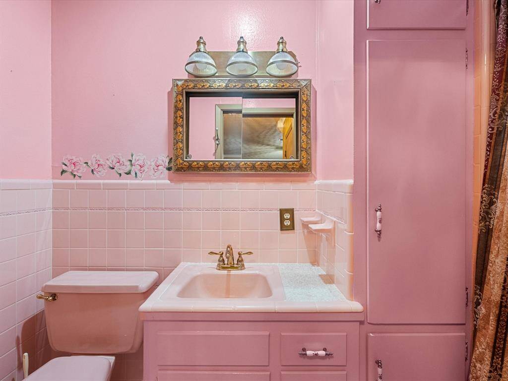 Oh-so charming retro style primary bath with pink tile and walls, a vintage mirror with decorative framing, brass fixtures, and stall shower. Tile-lined, built-in cabinetry offers additional storage .