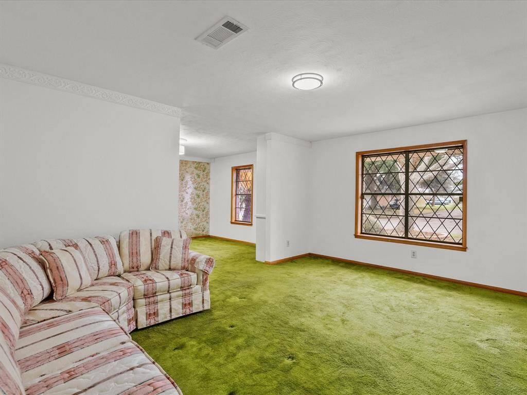 This spacious living room features bright green carpet and a large window with a grid pattern, allowing plenty of natural light.  Walls are a neutral white, providing a versatile backdrop.  Formal living seamlessly flows to a formal dining area.