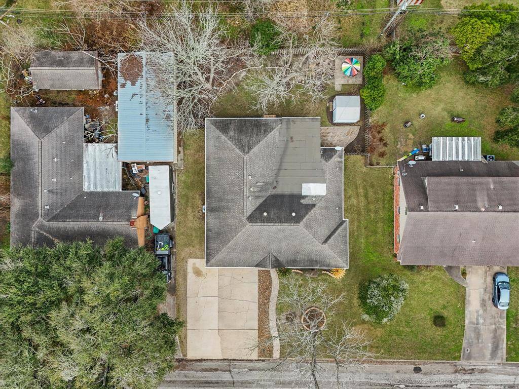Aerial pic showcases this residential property with a central house, a spacious driveway, and a fenced backyard. The backyard includes a small utility/storage shed and mature trees, providing privacy and a pleasant outdoor space. Located in the well-established neighborhood of Briar Meadow in La Marque, Tx
