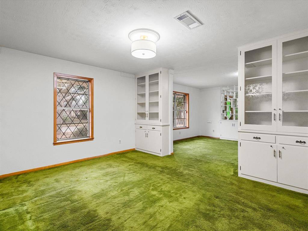 Showcasing a spacious, brightly-lit formal dining area. It features a large window with decorative grid patterns and custom built-ins - upper doors with glass fronts and bottom locking cabinetry for storage. A beautiful & functional, flexible-use space.