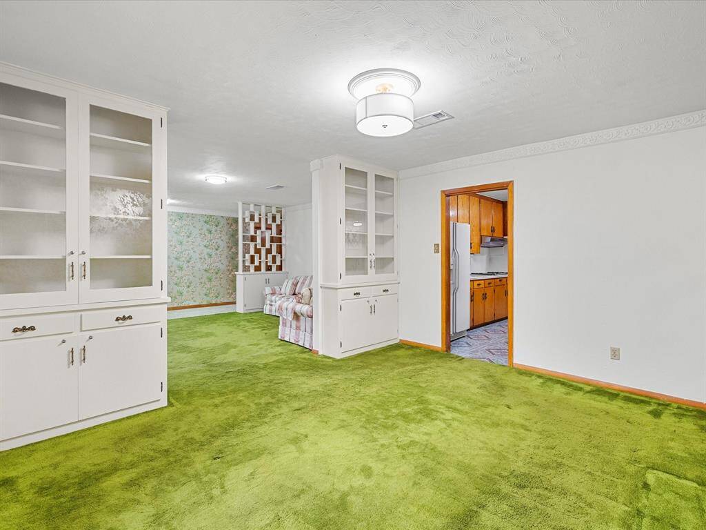 Adjacent to the formal living area, this formal dining features custom built-ins with upper glass-front and lower cabinets with lock-n-key. The formal dining area offers easy access into a retro-style kitchen with wood cabinets.