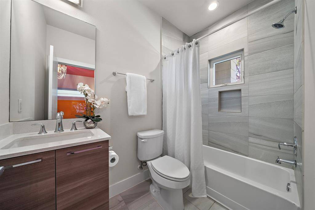 Featuring a chic tub/shower combo, this modern bath is designed with sleek fixtures and a spacious vanity. Neutral tile work and contemporary finishes create an inviting and stylish atmosphere.