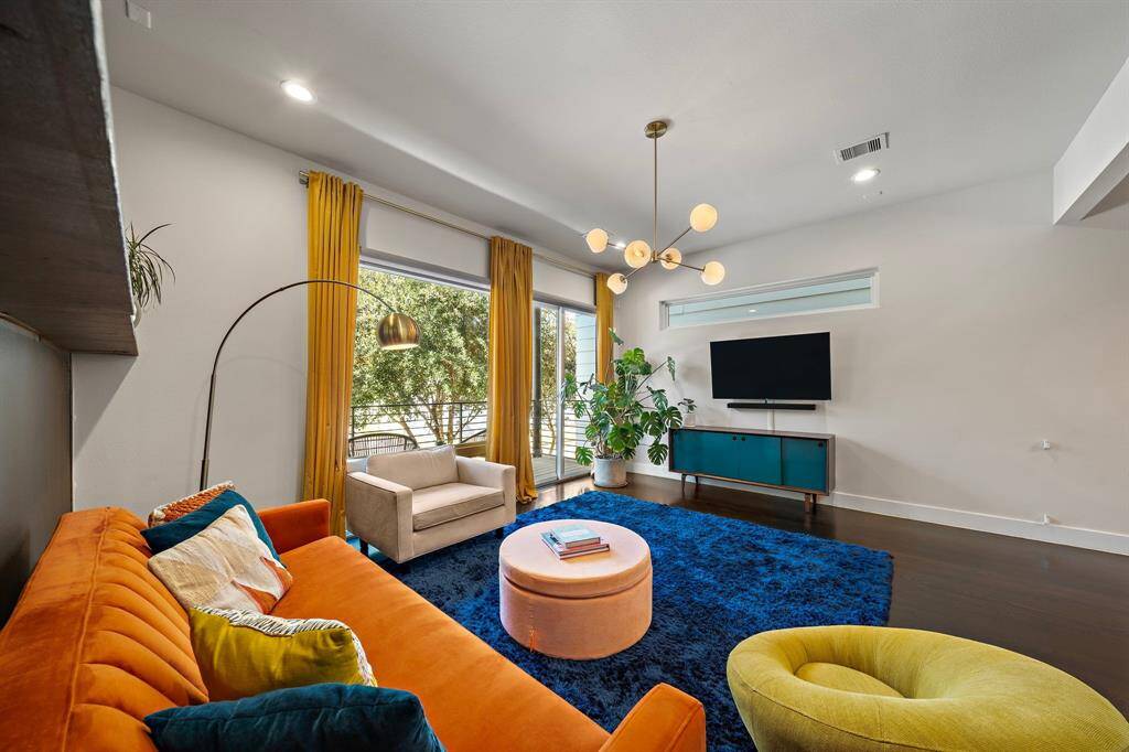 The vibrant living area features an open layout with high ceilings, designer lighting, and expansive windows that fill the space with natural light. Enjoy seamless indoor-outdoor living with access to a private patio and balcony, complemented by elegant hardwood floors.