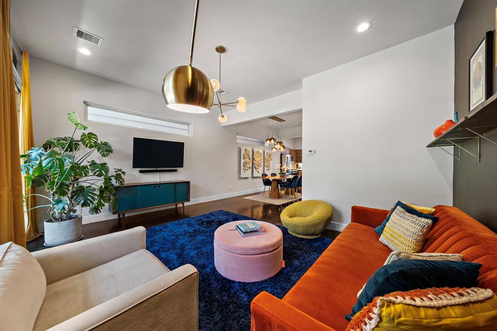 Contemporary elegance meets comfort in this living area, featuring vibrant decor and premium hardwood floors. Abundant natural light streams through expansive windows, highlighting the seamless flow between the dining and kitchen areas, ideal for relaxed evenings and entertaining.