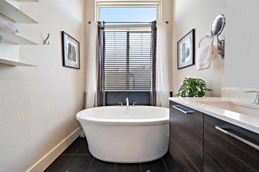 Indulge in modern luxury within this primary bath featuring a freestanding soaking tub beneath a large window, providing a serene escape. The dual sink vanity and sleek cabinetry enhance the contemporary design, while elegant fixtures and minimalistic decor complete this spa-like retreat.