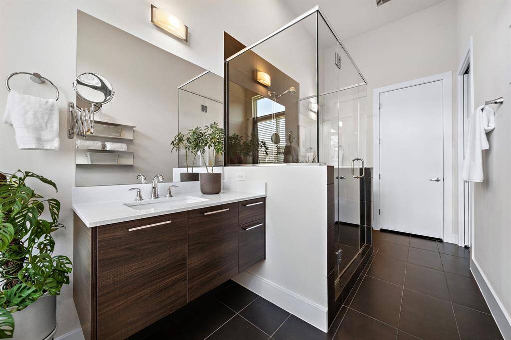 The primary bath features a sleek dual sink vanity and a glass-enclosed shower, enhancing its modern style. Contemporary tile flooring and elegant finishes complete this luxurious retreat, offering a space for relaxation and daily comfort.