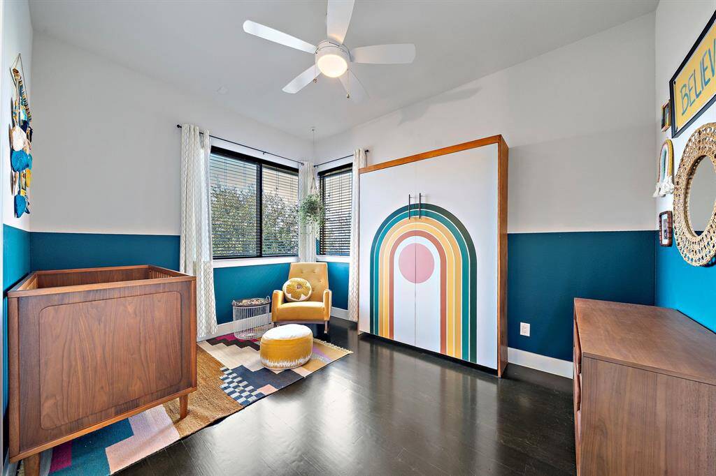 The secondary bedroom presents a vibrant and cozy space, inviting personalization. Large windows fill the room with natural light, highlighting the modern decor and bold color accents. Designed as a stylish and functional retreat, the room offers ample space for comfort and creativity.
