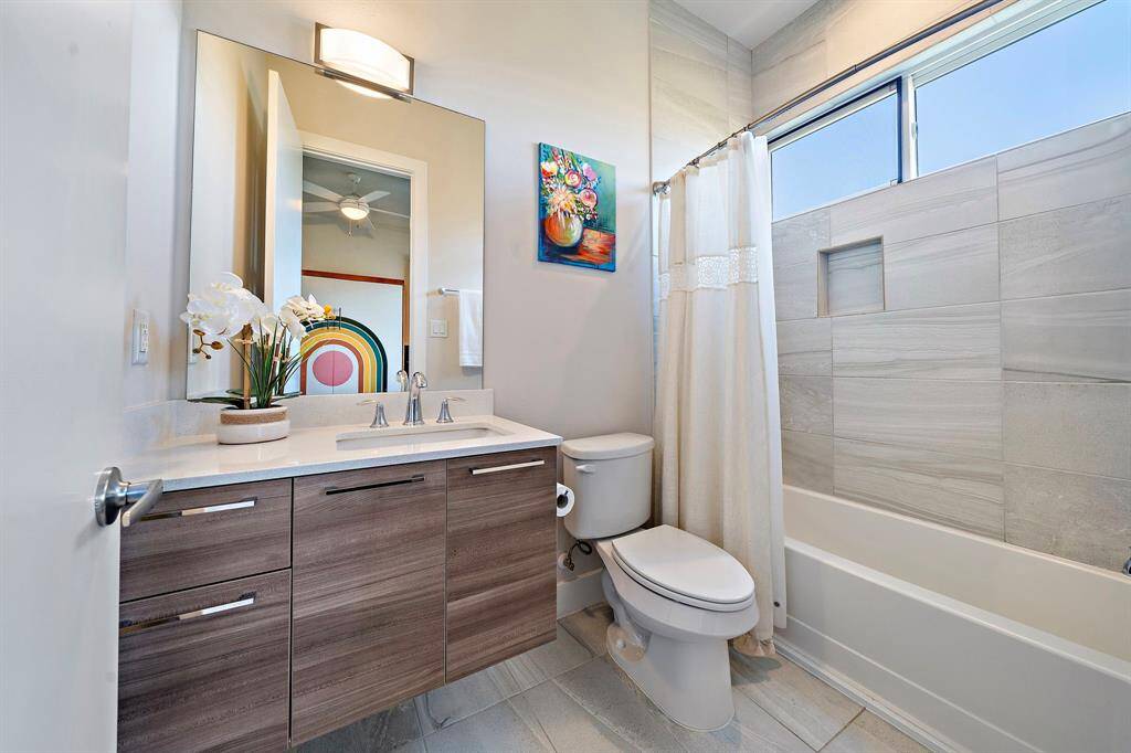 This modern secondary bath features a sleek vanity with a large mirror and ample storage. The tub/shower combo is finished with elegant tile, while contemporary fixtures add sophistication, creating a space that's both functional and stylish in this contemporary home.