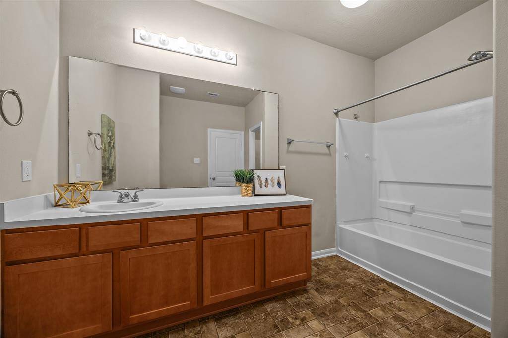 This bathroom features a spacious vanity with ample storage, a large mirror, and bright overhead lighting. It includes a  bathtub with a shower, and has a neutral color scheme for a modern feel.