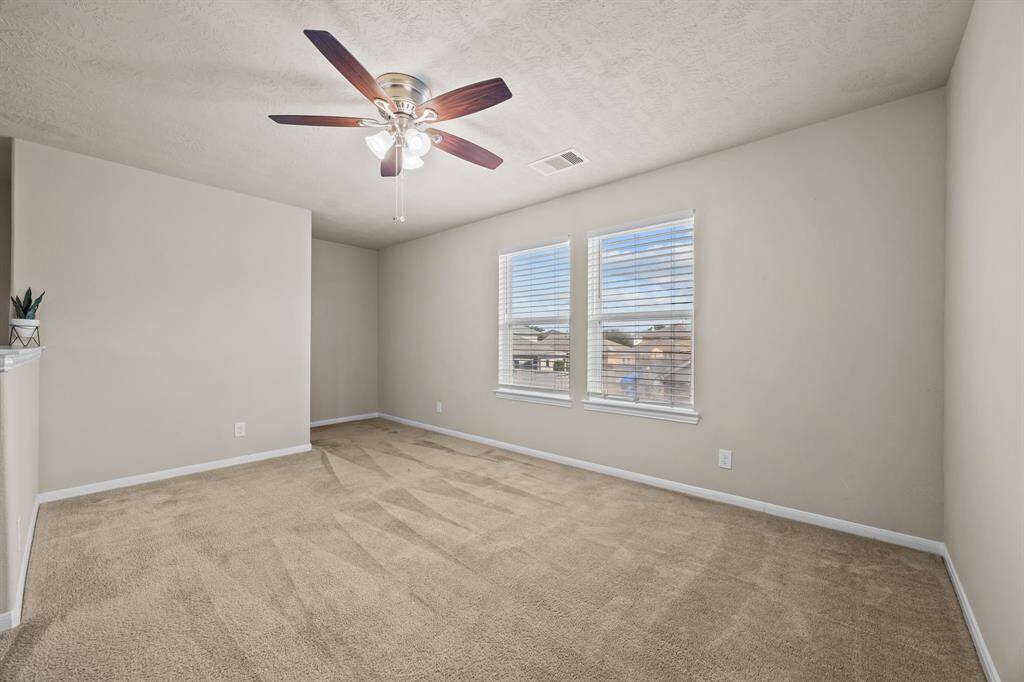 Spacious game room with plush carpeting, abundant natural light, and a stylish ceiling fan—perfect for recreation and relaxation.
