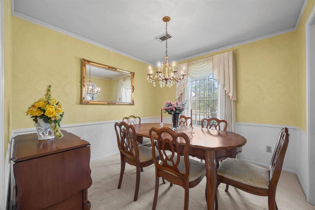 This Dining Room features elegant yellow walls with white wainscoting, and a decorative Chandelier. A large window with draped curtains provides natural light, complementing the traditional decor.