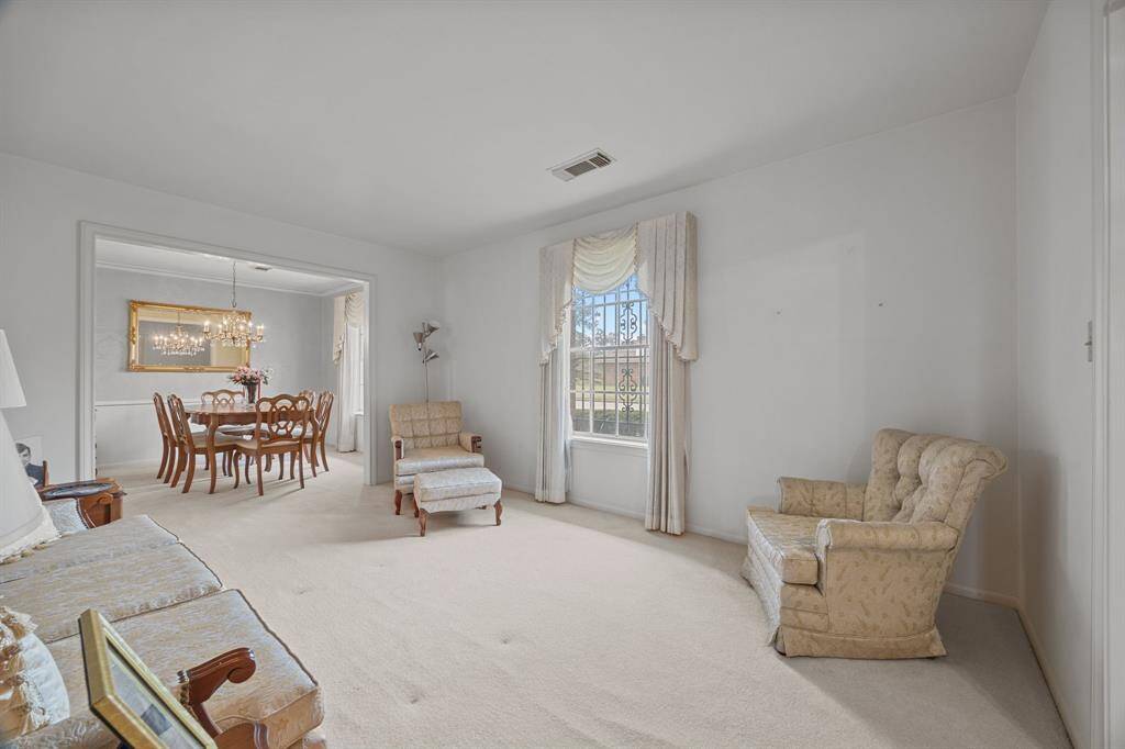 The Living Room is bright and carpeted, featuring a window with elegant drapery. Adjacent is a Formal Dining area with a Chandelier and a large mirror, creating a warm, inviting atmosphere.