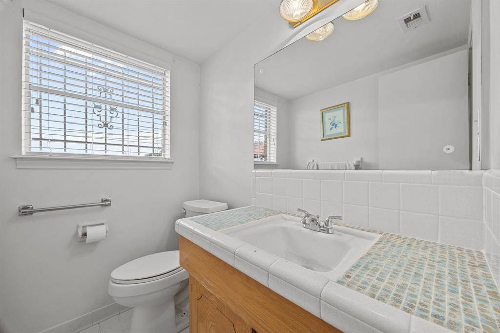 Downstairs 1/2 Bathroom has natural light, featuring a large mirror, tiled countertop, and a window with blinds.