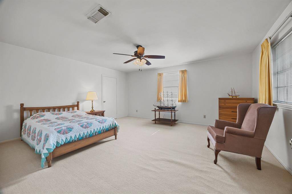 This spacious Bedroom features neutral carpeting, a ceiling fan, and large windows with curtains for natural light. Perfect for a comfortable and inviting atmosphere.