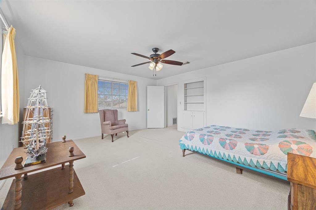 Bright and spacious Bedroom with neutral walls and carpet, featuring a ceiling fan, large window with curtains, and ample natural light.