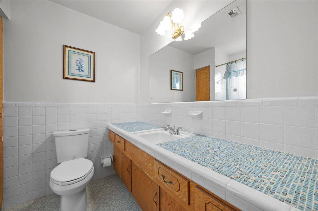 This Primary Bathroom features a clean, classic design with white walls and a long countertop with blue mosaic accents. It has a large mirror, wooden cabinetry, and a bright, inviting atmosphere.