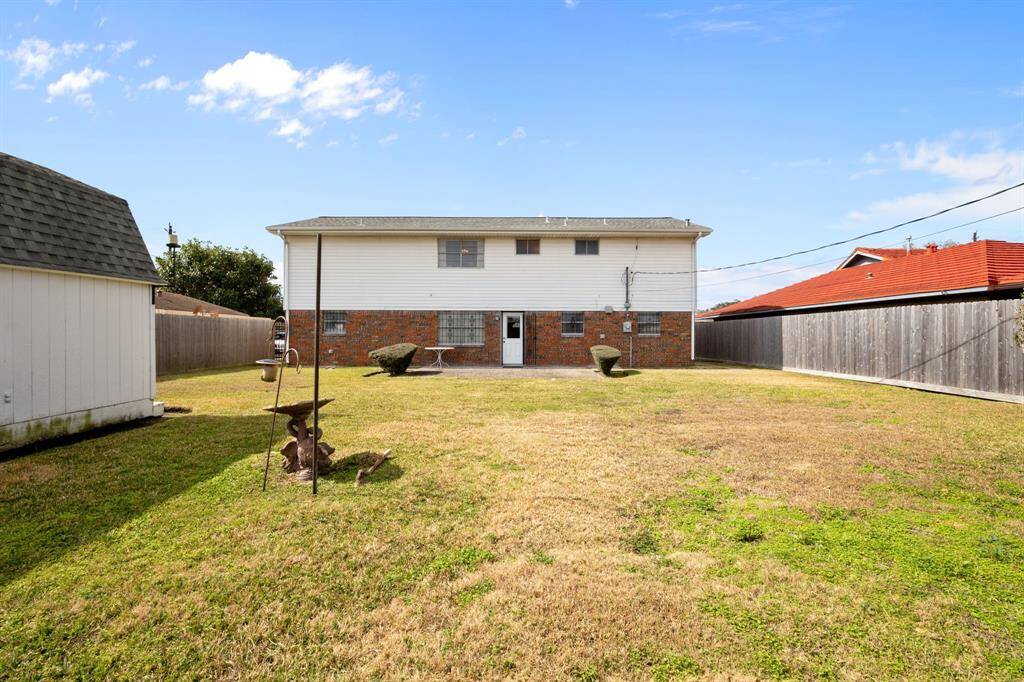 Spacious Backyard with a two-story brick House, featuring a well-maintained lawn and a Storage Shed on the left. The yard is fenced for privacy.