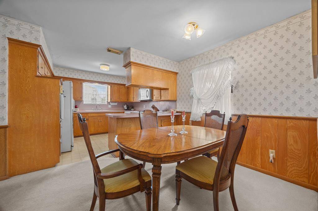 Cozy Breakfast Room is connected to the Kitchen. It features warm wood cabinetry and patterned wallpaper, creating a vintage charm. A large window allows natural light to brighten the space.