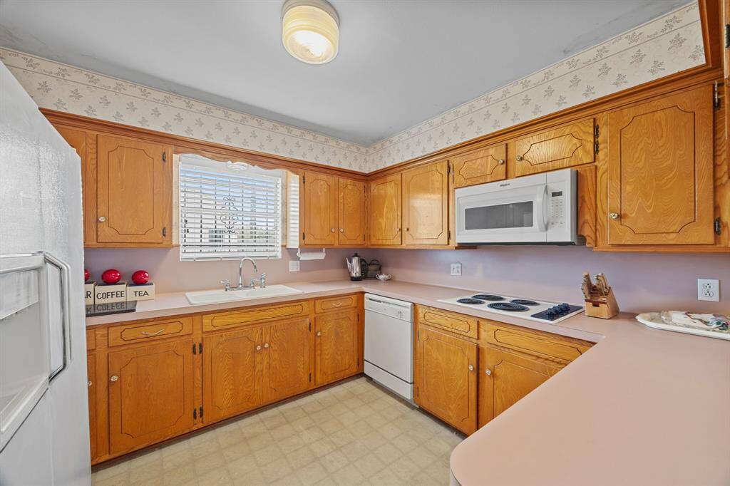 This Kitchen features warm wooden cabinetry, a built-in Microwave, and a Dishwasher. It has a cozy feel with a large window for natural light and a functional layout with ample counter space.