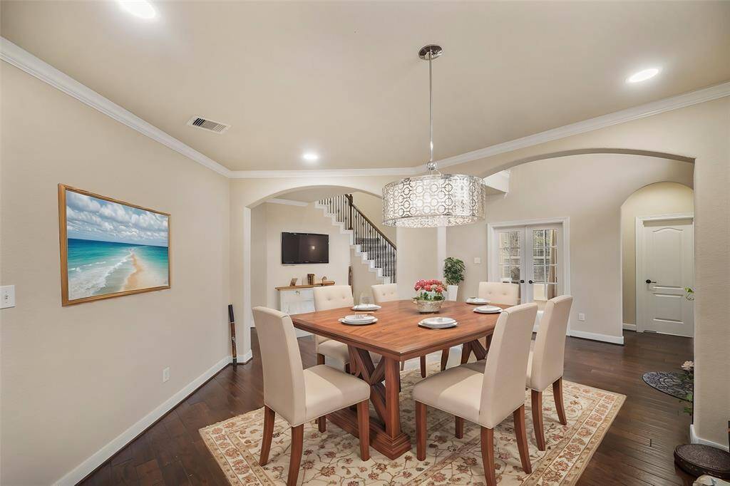The dining room showcases stunning rich wood floors, complemented by elegant crown molding. A sleek modern chandelier serves as the centerpiece, casting a stylish glow over this sophisticated space.