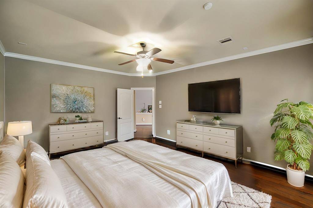 The primary bedroom boasts rich wood floors and elegant crown molding. A wall of windows showcases stunning views of the backyard and sparkling pool, filling the space with natural light and tranquility.