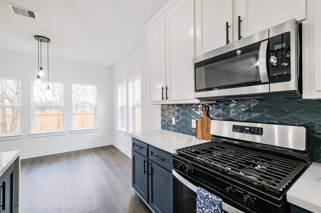 This kitchen features modern design with white upper cabinets and navy lower cabinets, complemented by a sleek marble countertop. The stylish blue geometric tile backsplash adds a touch of elegance, while a double sink sits beneath a large window, offering ample natural light.