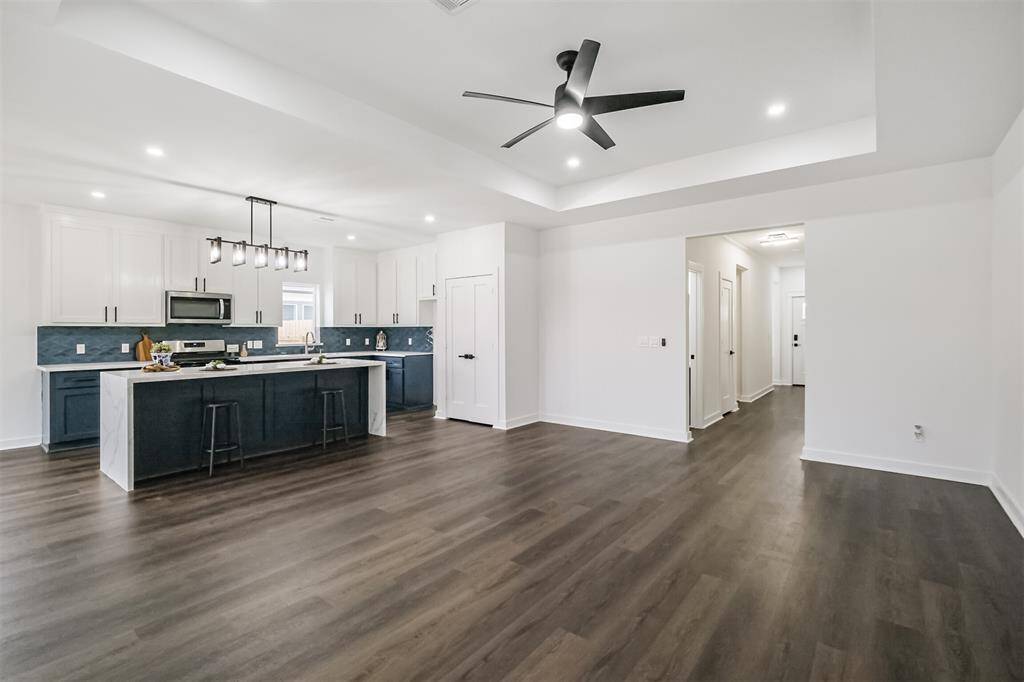 Modern kitchen with sleek white and navy cabinetry, stainless steel appliances, and a large island with seating. The space is bright, featuring recessed lighting and a contemporary pendant fixture. Dark wood flooring adds warmth, and ample windows bring in natural light.