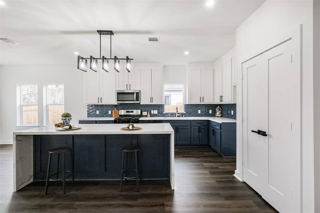 Bright dining area with large windows, modern pendant lights, and hardwood floors. Great natural light and a view of the fenced backyard.