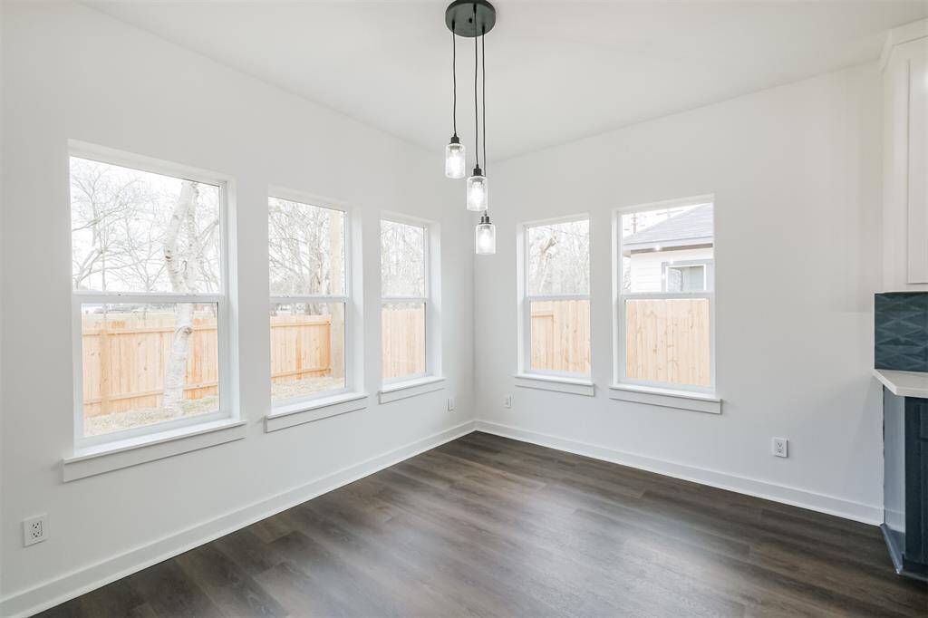 Bright and airy room featuring large windows, modern lighting, and dark wood flooring. The space is enhanced by a white door and walls, offering a clean and inviting atmosphere.
