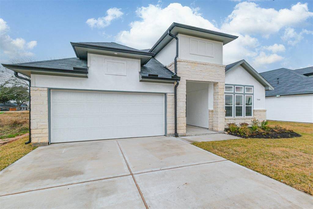 This modern home features a clean, contemporary design with a light stone exterior and dark roof. It has a spacious two-car garage and a well-maintained front yard. Large windows provide ample natural light.