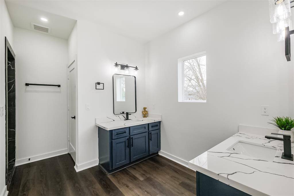 This room features clean white walls and dark wood flooring, complemented by a modern ceiling fan. It has ample natural light and two doorways, offering a spacious and airy feel.