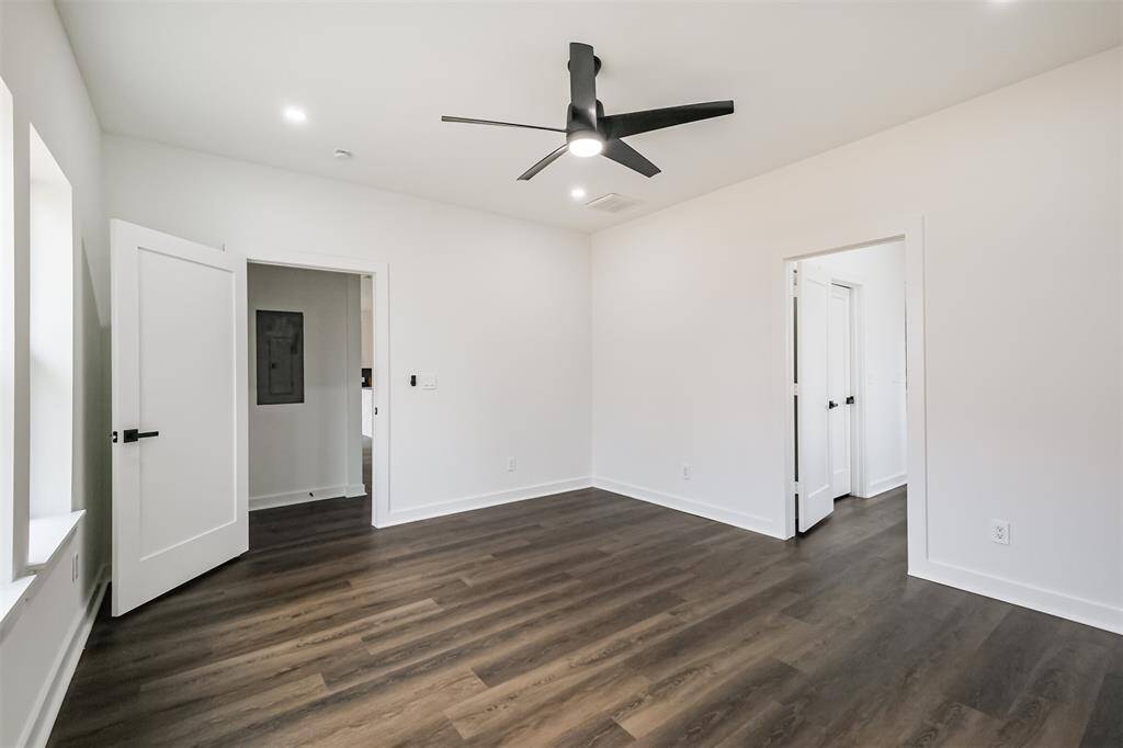 This room features clean white walls, dark wood flooring, and a modern ceiling fan. It has recessed lighting, a window for natural light, and an adjoining bathroom.