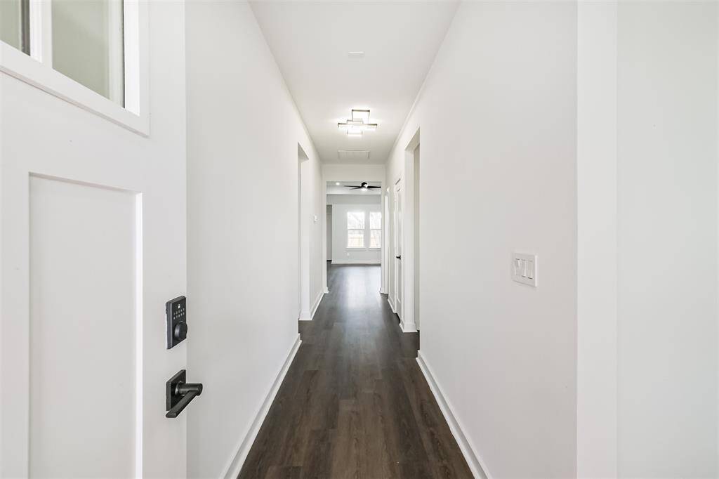 This spacious living room features elegant dark wood flooring, a modern ceiling fan, and recessed lighting, creating a bright and inviting atmosphere. The room's neutral walls and large windows offer ample natural light, perfect for any style of decor.