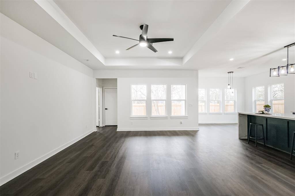 This photo showcases a modern, open-concept living space with dark wood flooring, a sleek kitchen featuring a large island, and ample natural light from multiple windows. The area is accented by recessed lighting and a ceiling fan, creating a bright and inviting atmosphere.