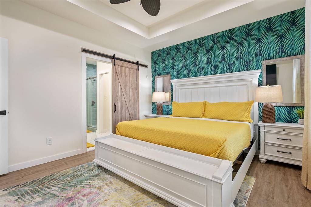 The windows provide ample natural light to the primary suite, which has a trayed ceiling, fan, and wall mural. There's plenty of room even with the king bed with built-in storage bench.