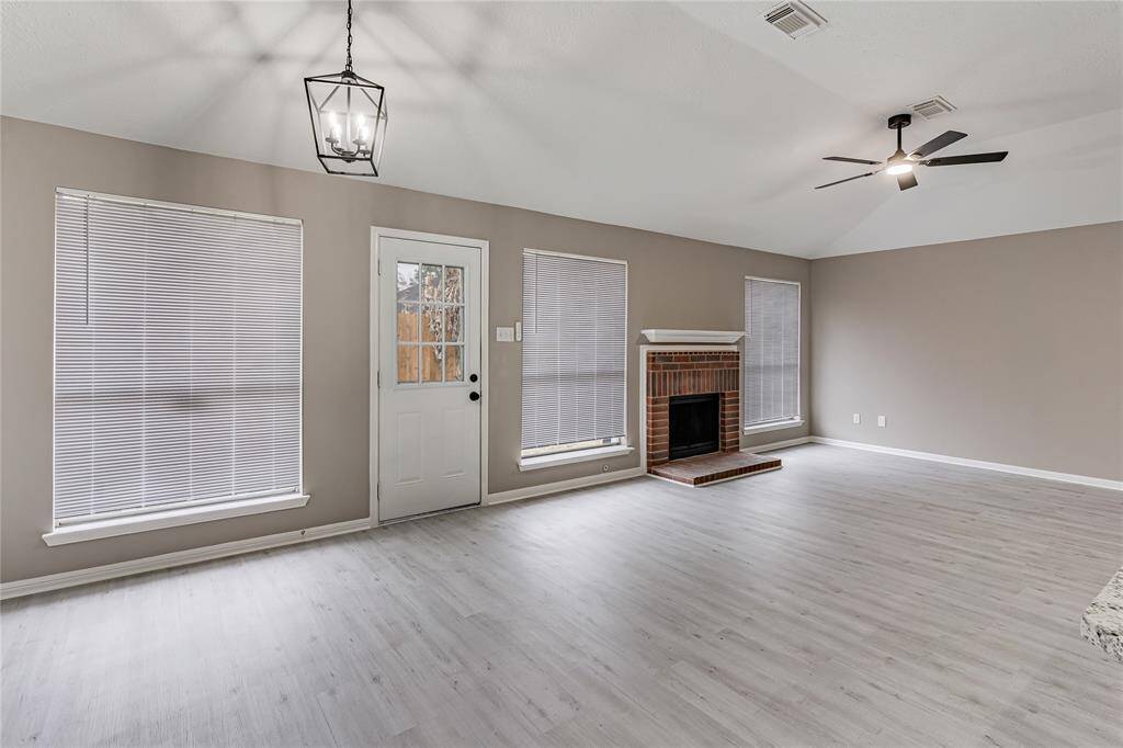 Bright and inviting living area with vaulted ceilings, modern fixtures, and a cozy brick fireplace. Perfect for relaxation and gatherings.
