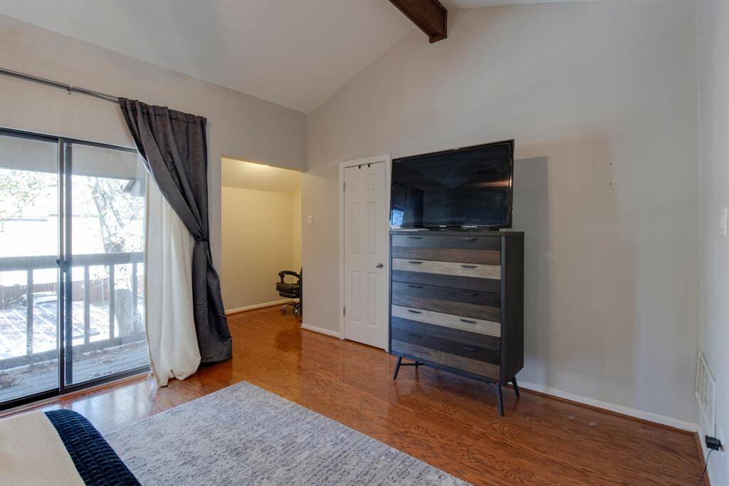 Primary bedroom has vaulted ceiling with wood beam ceiling accent, ceiling fan and office nook to the right of the  balcony.