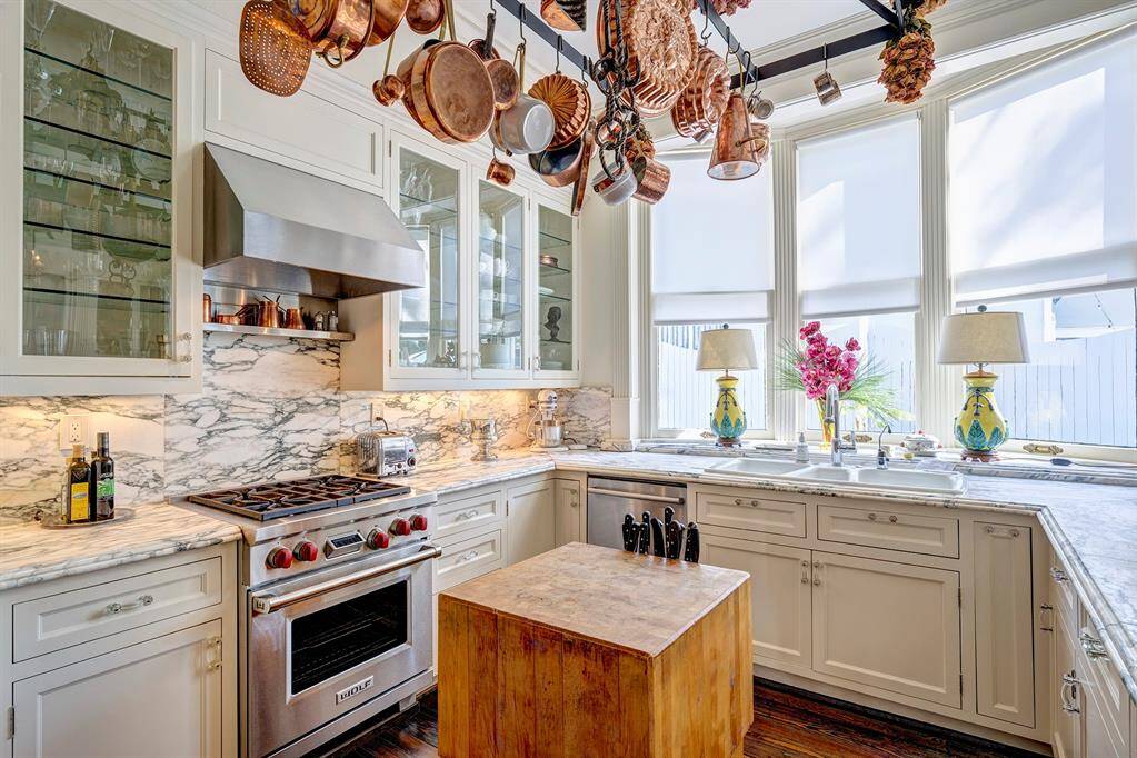 The kitchen is a stunning fusion of elegance and functionality, designed to inspire culinary creativity. Large windows frame picturesque views of the sparkling pool and meticulously landscaped backyard, infusing the space with natural light and a serene ambiance. At its heart is a professional-grade Wolf range, perfect for crafting gourmet meals, complemented by expansive marble countertops that offer both beauty and durability.