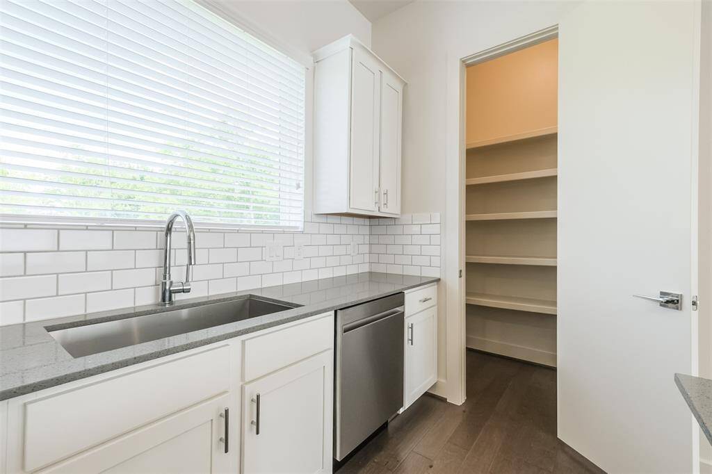 The large window not only offers a scenic view of the outdoors but also frames the stainless steel dishwasher and walk-in pantry.