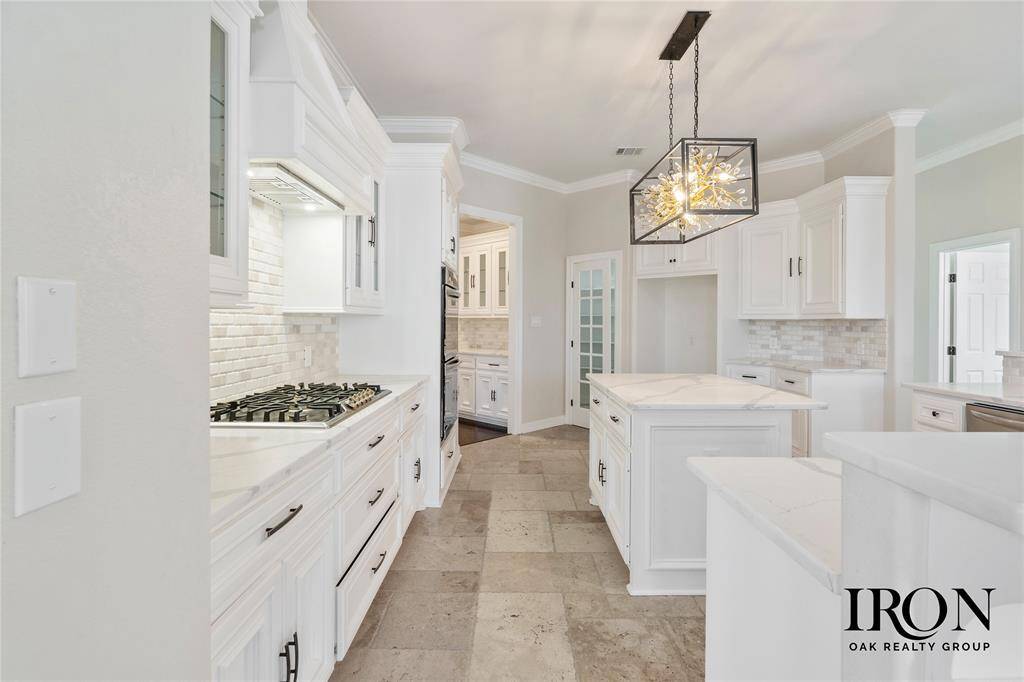 Another view of the stunning kitchen showcasing high-end stainless steel appliances, including double ovens and a built-in microwave. The combination of classic white cabinetry, quartz countertops, and contemporary lighting fixtures creates a perfect blend of modern luxury and timeless charm.