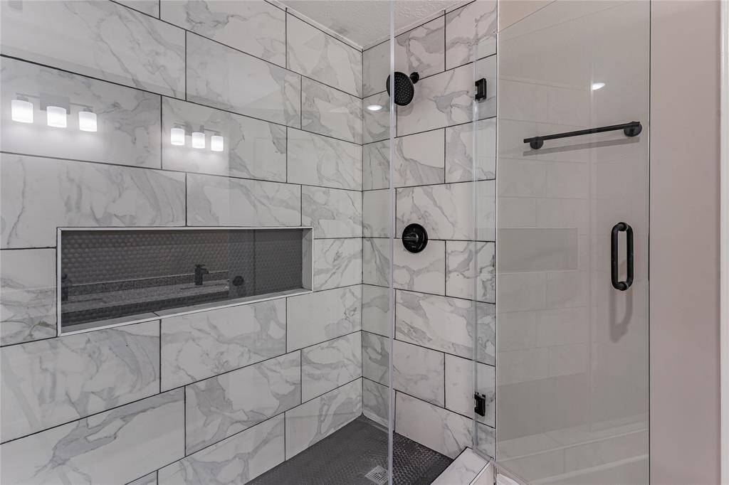 Luxurious primary bath featuring elegant marble tile and a sleek glass-enclosed shower.