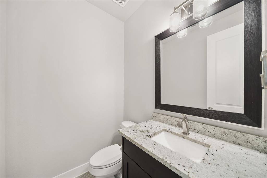 Convenient for guests, the second floor half bath includes wood-stained cabinetry with a granite counter top and integrated back splash accompanied by a wood-stained framed mirror with lighting above.