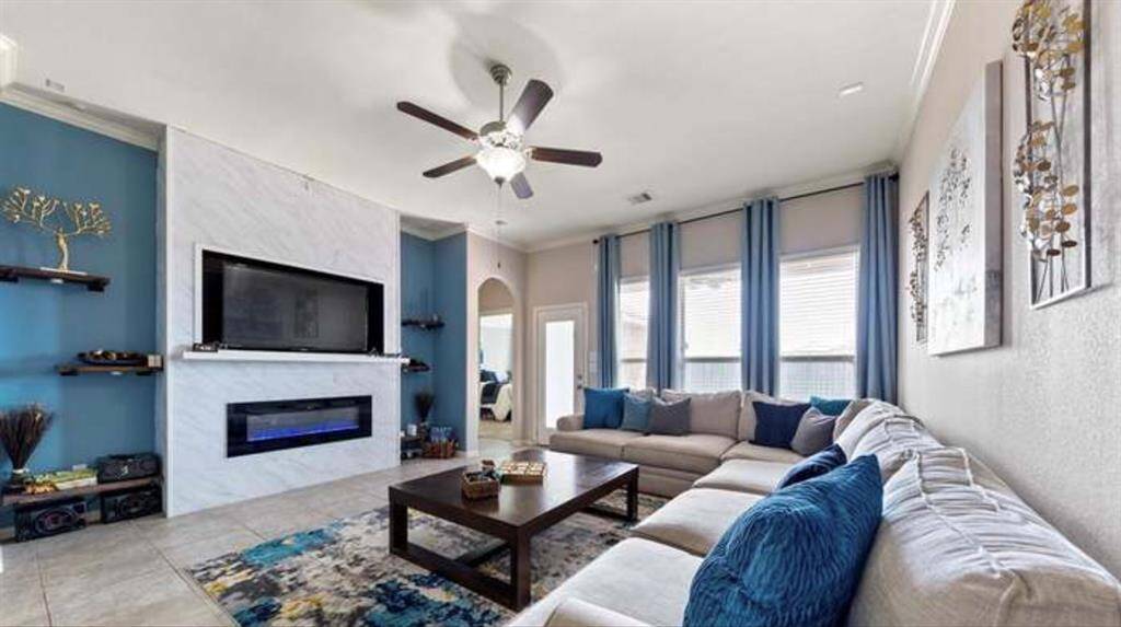 This living room features a spacious and modern design. It has a sleek fireplace, complemented by built-in shelves. Large windows provide ample natural light, and the ceiling fan adds comfort.