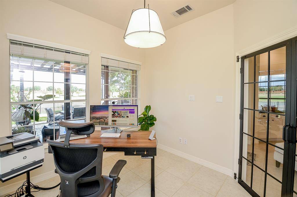 This photo shows a bright home office with large windows offering a view of a patio and greenery.  The room is separated by glass doors, providing a quiet workspace.