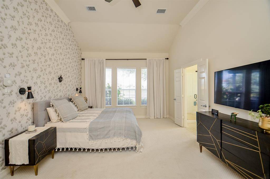 This spacious primary suite is just off the living room. Vaulted ceilings, new carpet (2024) and subtly chic wallpaper create this elegant space.  Three large windows overlook the back yard. French doors lead to the spa like bath.